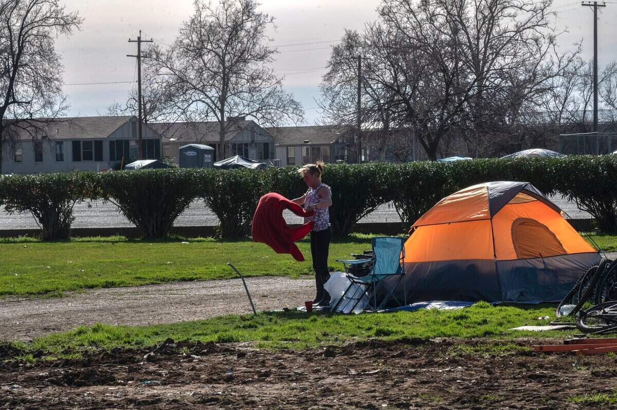 Vikki Emrick, 54, shakes out a blanket in January at a homeless encampment across the street from the north Auburn government center. “All of these fresh muddy spots are here from the tractor coming out, the bulldozer and scooping up people’s tents and their stuff and putting it in the garbage,” Emrick said.
