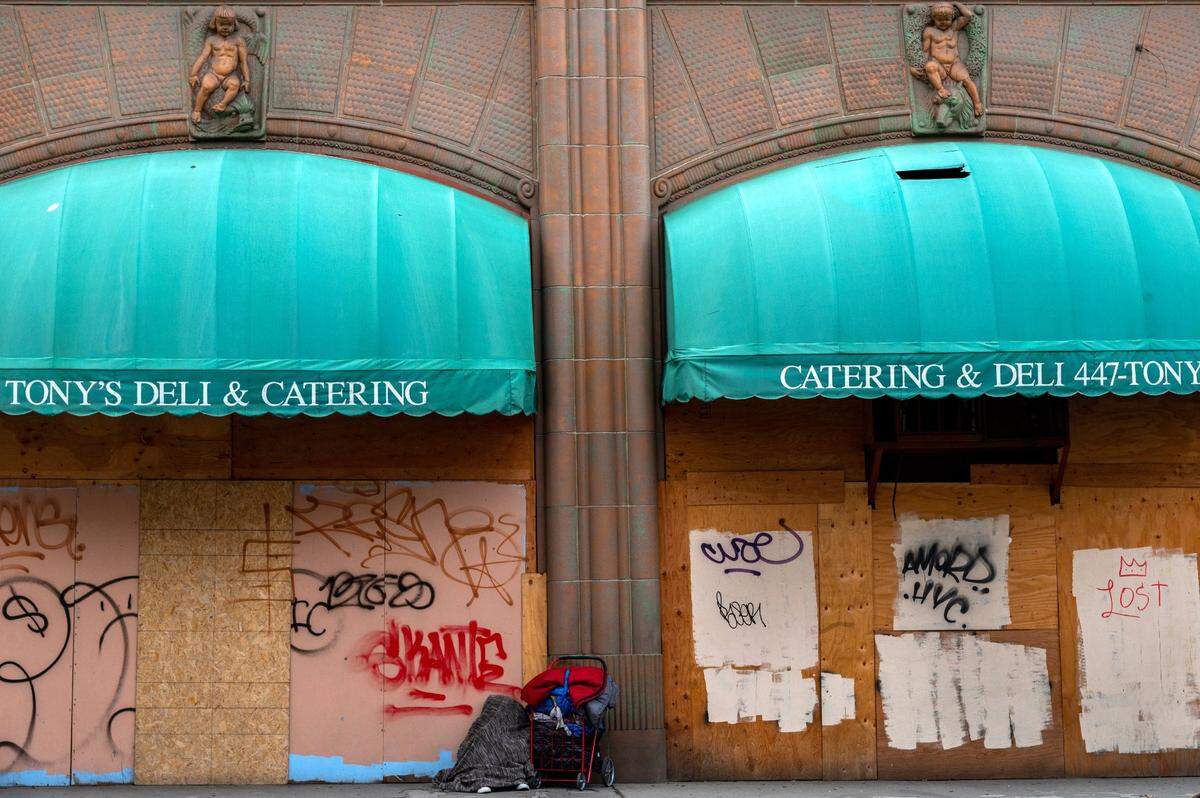 A homeless person rests next to a cart of belongings on 12th Street in front of boarded up windows in downtown Sacramento on Feb. 18. To the far right the graffiti says ”Lost.”