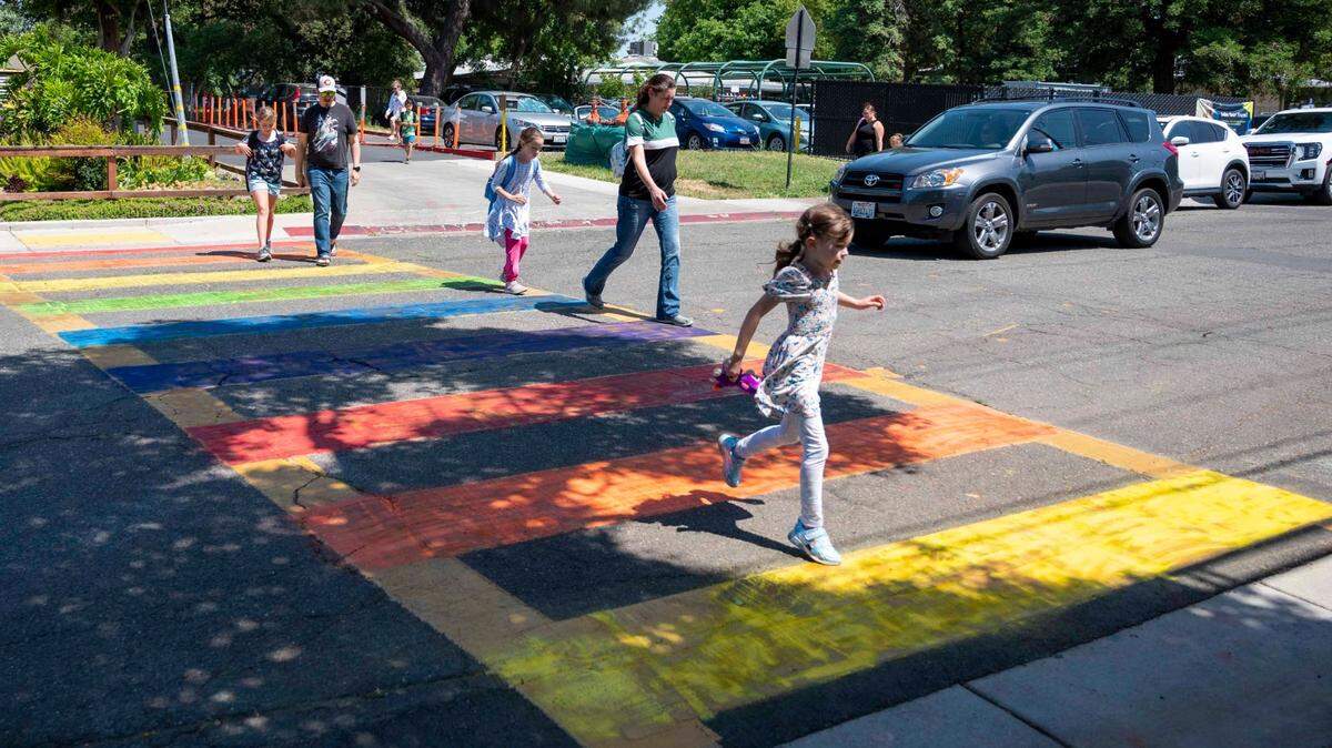 Parents and students cross the street at a rainbow-colored crosswalk across from Birch Lane Elementary School in Davis on Thursday, May 25, 2023. The crosswalk was painted for LGBTQ Pride month. City public works crews on Friday May 26, 2023, removed the rainbow chalk, since it was not authorized, and repainted the crosswalk.