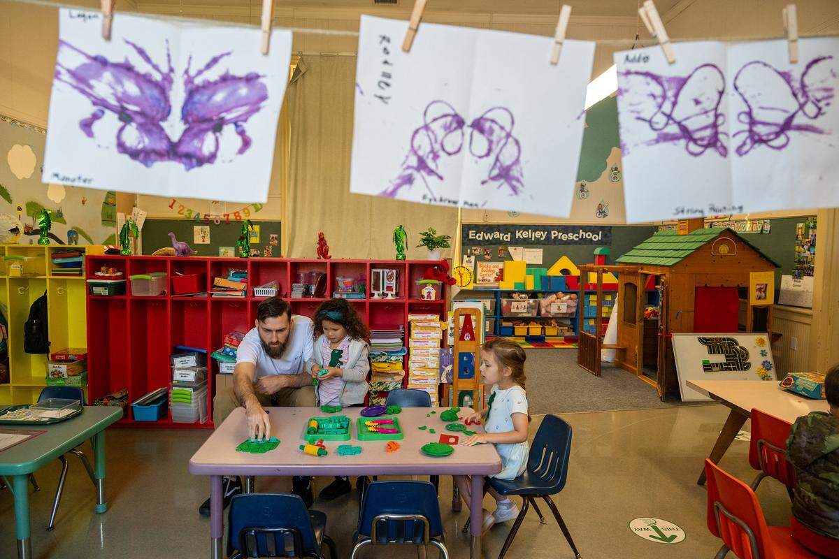 Parent Brian Hopkins helps students Liliana, 4, center, and Natalie, 4, right, make clay dinosaurs as they learn about prehistoric animals at Edward Kelley parent participation preschool in Rosemont on Thursday. Student artwork hangs above.