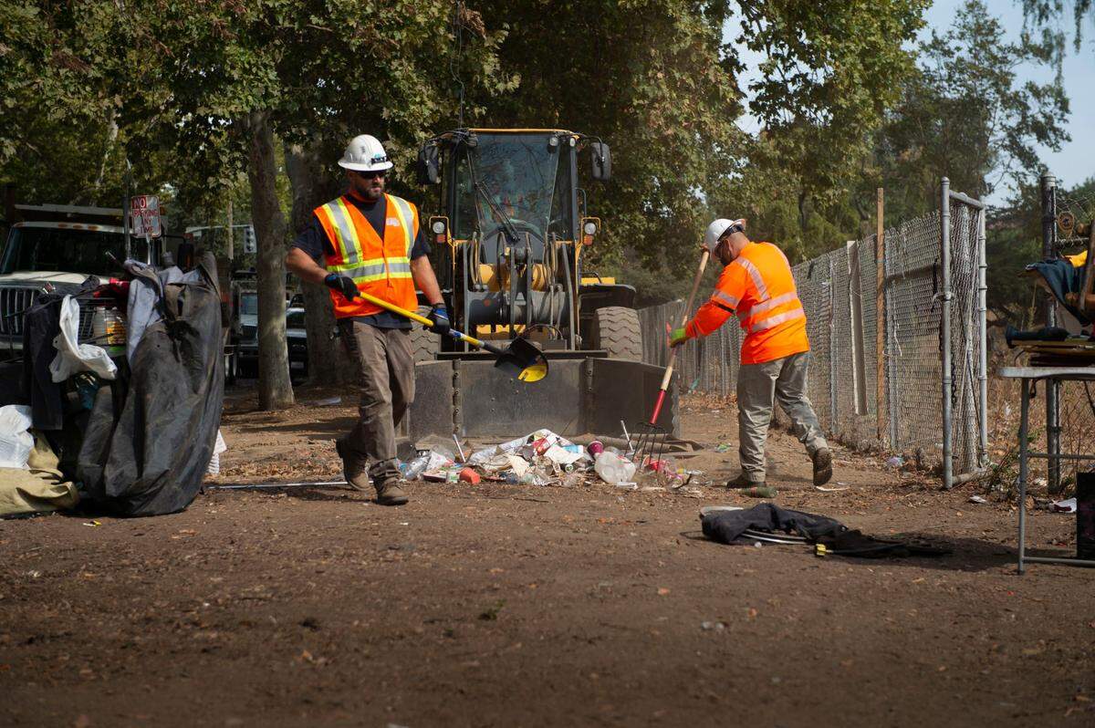 Caltrans workers clear a homeless camp at 29th and G streets in Midtown Sacramento near the Capital City Freeway in October 2021. The agency wants more than $5 million to help clear more encampments around the state.
