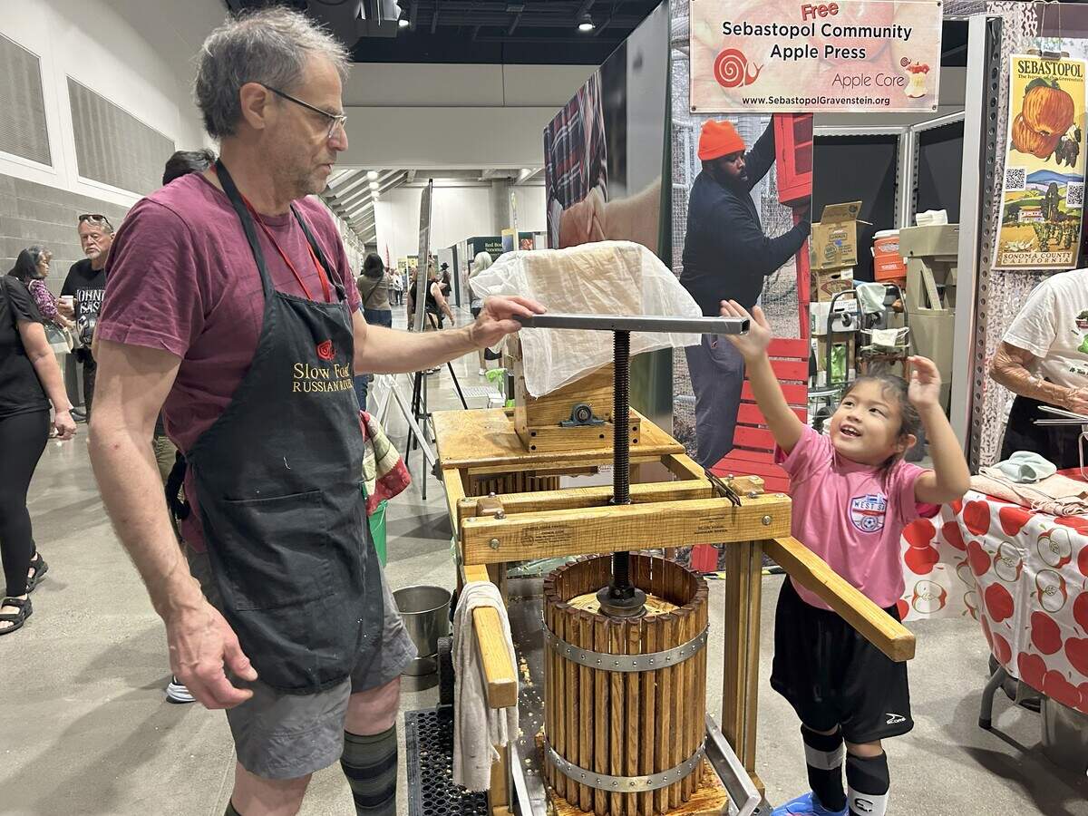 Harold Glasser, member of the Slow food Russian River organization, assists Skylar Foreman in pressing apples during the Terra Madre Americas event Saturday in Sacramento.