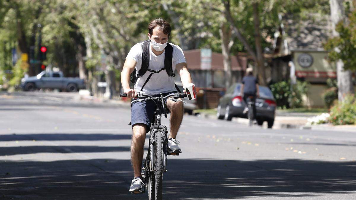 A bicycle rider wears a face mask as he travels through downtown Davis on Monday, April 27, 2020. Yolo County, where Davis is located, now requires people to wear face masks in public. Face coverings are not required for bicycling, running, walking, hiking or at home or alone in a car.