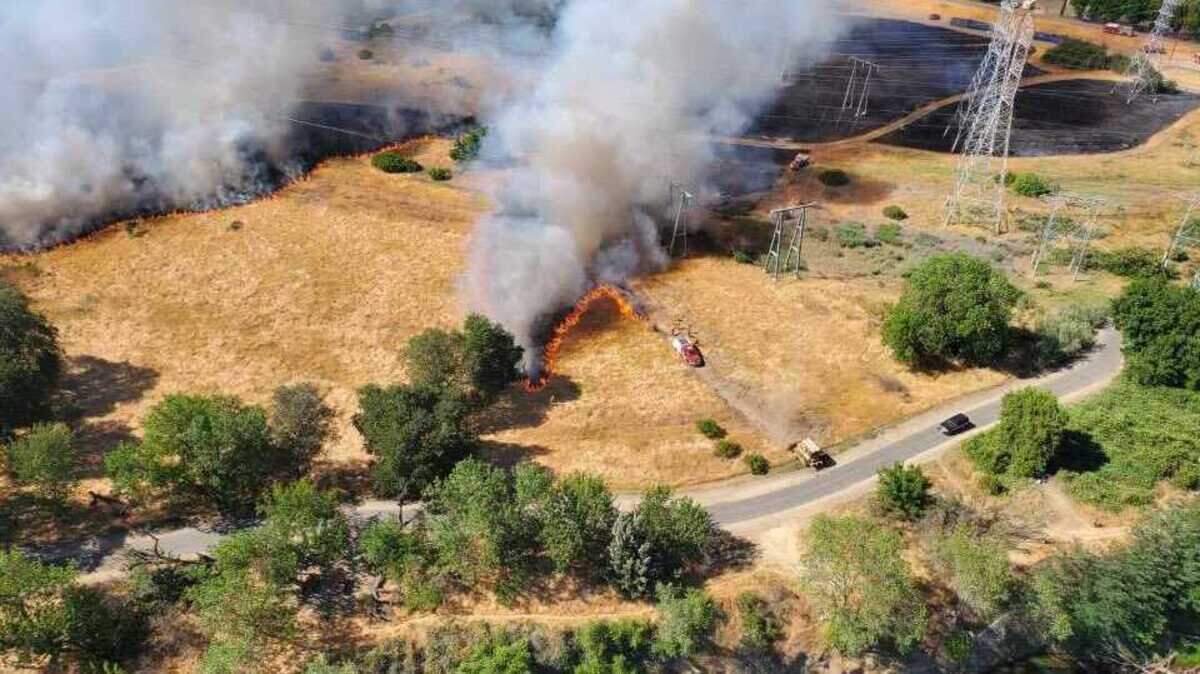 Fire crews are seen working on a grass fire in the American River Parkway in Sacramento, Calif., on Sunday, June 6, 2021. The brush fire charred between 75 and 100 acres and sent large plumes of smoke into the air.