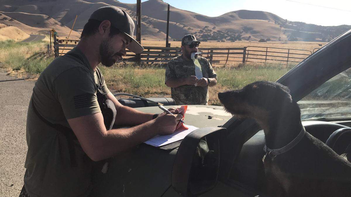 Sam McGuire, a wild pig hunting guide from Lockwood, enters his client's hunting license information into his log book on June 16, 2018. Looking on are Emma, McGuire's terrier, and his client, John Locatelli. A bill in the legislature would allow hunters to pay a flat annual fee to hunt pigs instead of buying a kill permit for each animal.