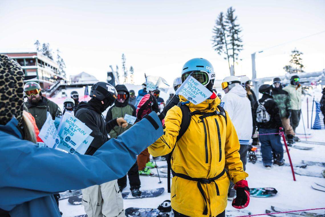 Skiers and snowboarders pick up commemorative flags at Sierra-at-Tahoe’s season opening on Saturday, Dec. 27, 2025. The resort welcomed guests back after a delayed start, offering opening-day giveaways and a DJ playing music at the base lodge.