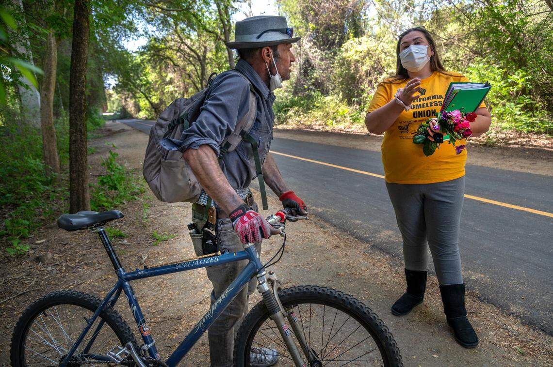 Crystal Sanchez, president of the Sacramento Homeless Union, chats with homeless resident Christopher Lamb on Wednesday, April 14, 2021, as she searches for a place to place flowers for a homeless woman was killed Saturday along the American River bike trail. Lamb wears a knife on his belt. ”Personally, I’m not too scared. Do I walk around with a weapon? Yes,” said Lamb, who is afraid for his wife because he says there is a group of people who take advantage of vulnerable people.