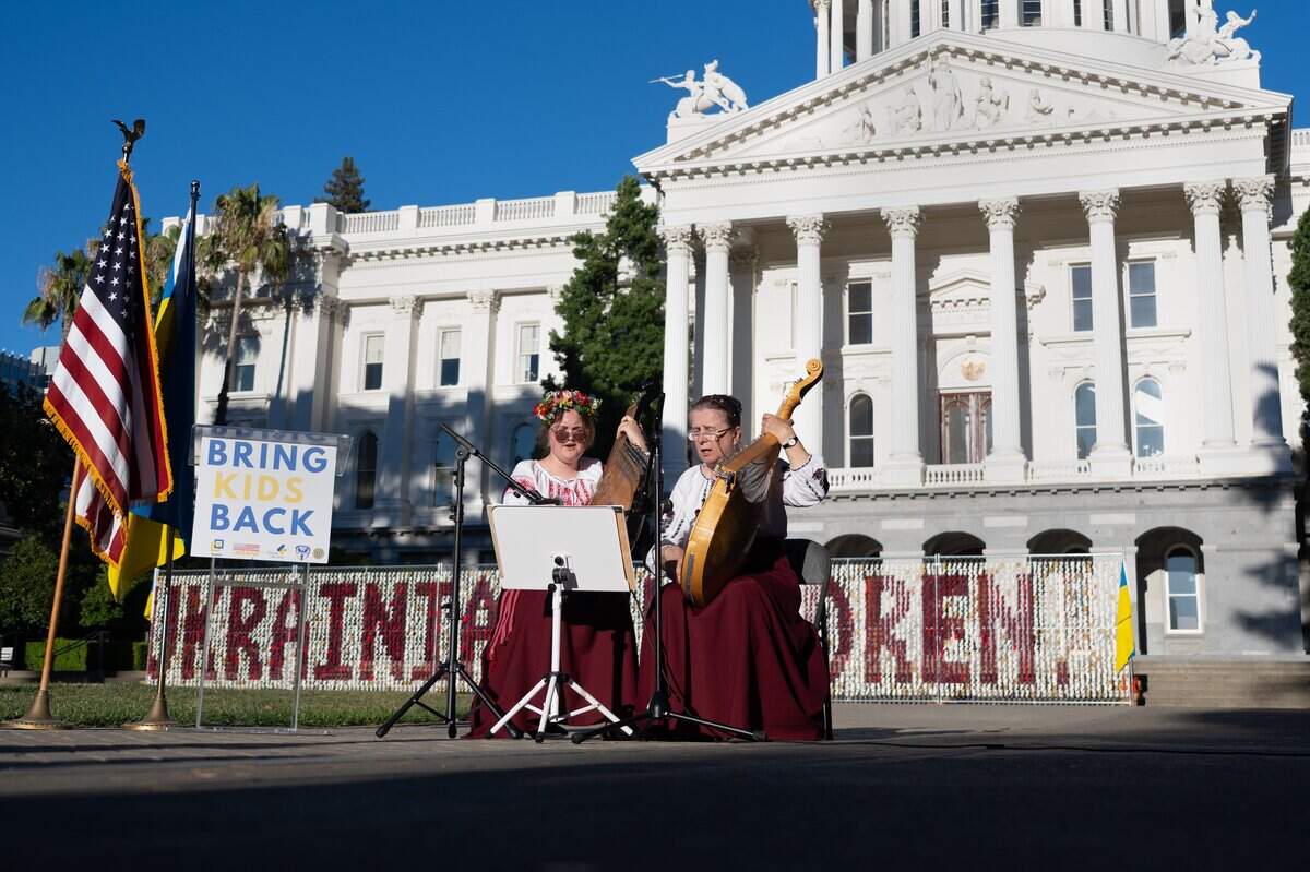 Olha Herasymenko, left, and Sophia Ishchuk, right, perform on banduras in front of the state Capitol on Monday. The bandura is a Ukrainian folk instrument that can have up to 65 strings. Behind them stands an installation of 20,000 teddy bears, each representing a Ukrainian child abducted by Russia.