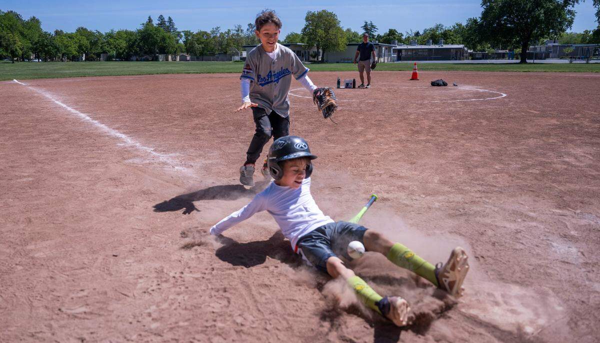 Franco Bugni, 10, chases his brother Tony, 8, as he slides at home base at Community Park in Davis the weekend after three people were injured when a shooting took place during Picnic Day. North Davis Elementary School stands in the background.