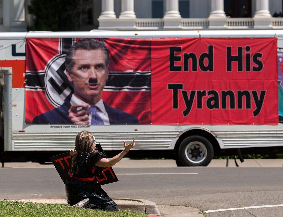 A banner at a Capitol protest against the coronavirus stay-at-home orders shows Gov. Gavin Newsom on a Nazi flag with an Adolf Hitler mustache on May 7, 2020.