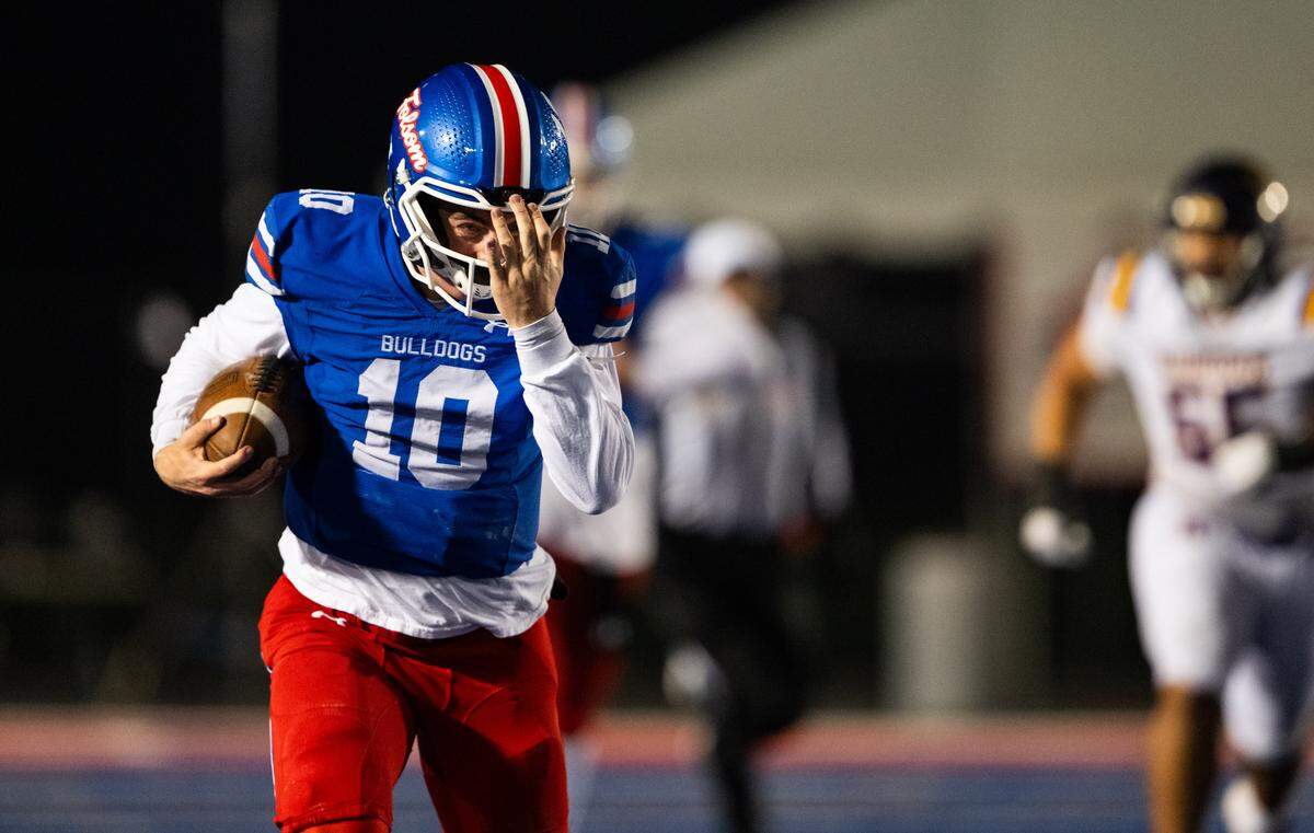 Folsom Bulldogs quarterback Brody Rudnicki (10) adjusts his loose helmet as he rushes down the sideline for 50 yards against the Riordan Crusaders In the CIF Northern California Regional Division 1-AA football championship game in Folsom on Friday.
