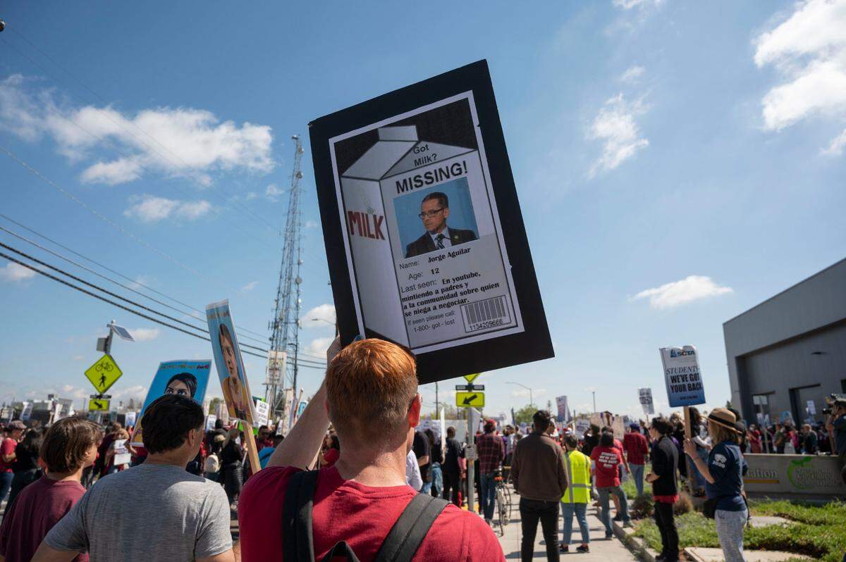 Kindergarten teacher Will Kilfoyle holds a poster that he printed from a meme he found on Facebook duirng a teachers’ strike rally Tuesday. The sign reads in Spanish, “Last seen: In YouTube lying to parents and to the community with who he refuses to negotiate.”