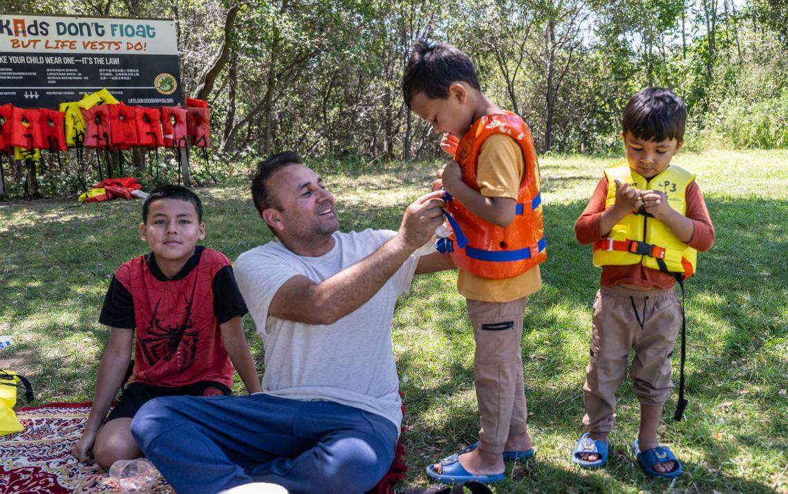 Noorullah Jambi of Sacramento helps his sons Shahab, 5, and Jason, 3, with their life vest on June 27, 2024, before playing on the American River at River Bend Park in Carmichael on as oldest brother Orfan, 11, left, waits. Life jackets are available for the public along the American River Parkway.