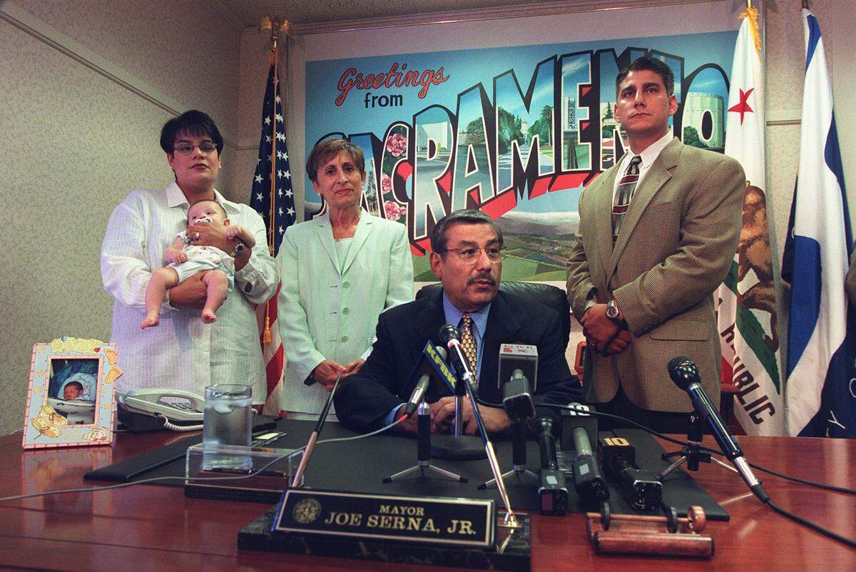 Then-Sacramento Mayor Joe Serna Jr. responds to questions from the media in his City Hall office in 1999 regarding the cancer that has reappeared in his body. Behind Serna, from left, are daughter Lisa Mayorga holding her two-month-old son, wife Isabel Serna and son Phil Serna.