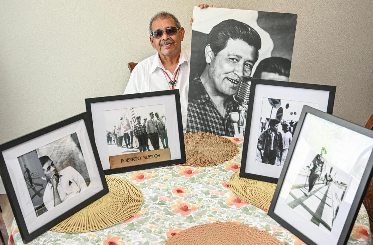 Roberto Bustos of Tulare, best known as “El Capitan” during the United Farm Workers march of 1966, sits with several photos of himself during the march and with UFW leader Cesar Chavez at his home on Saturday.