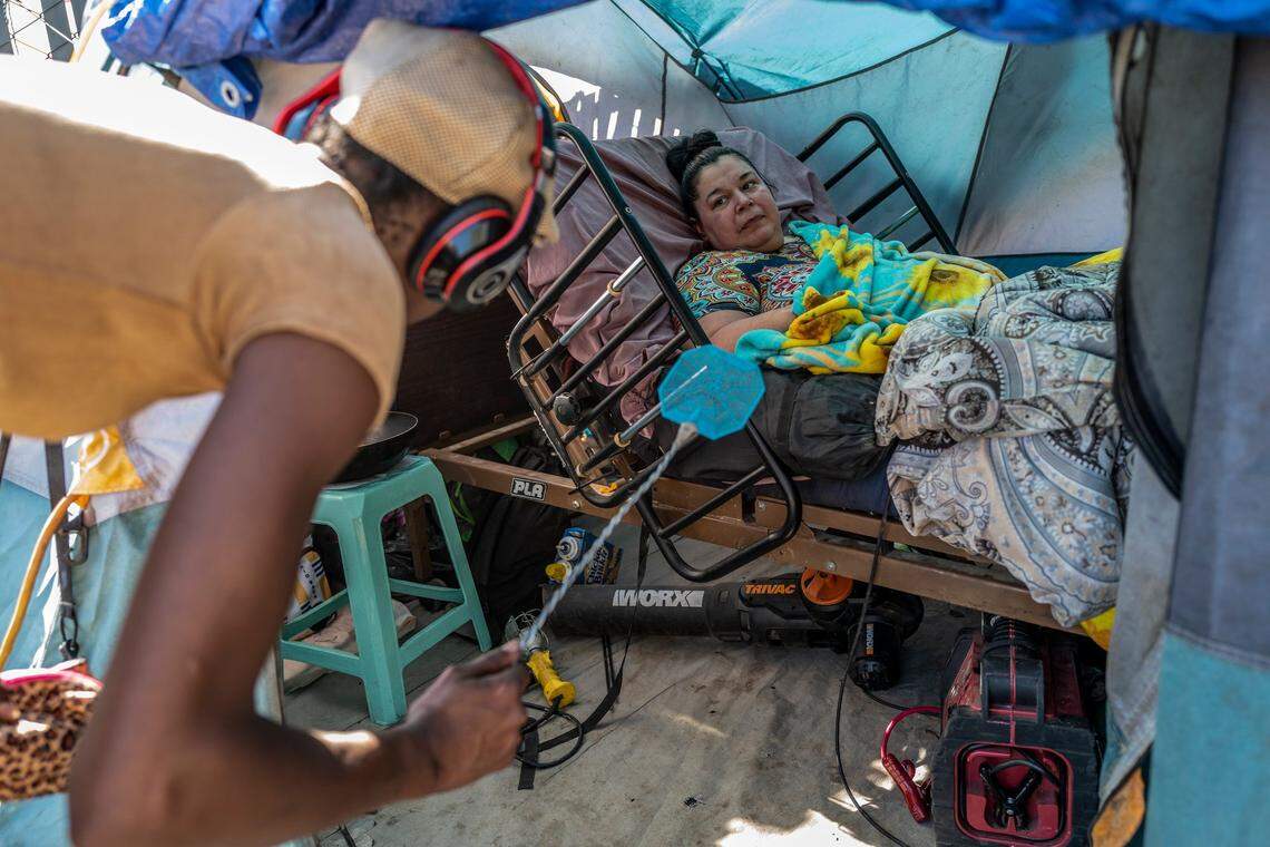 A homeless resident of Camp Resolution swats flies inside Holly Porter’s tent in Sacramento in October. Porter, who suffers from quadriplegia and only has limited movement in one hand, is unable to swat the flies that land on her face. She moved back to the encampment on Colfax Street after advocates from Oakland and Sacramento reclaimed the lot.