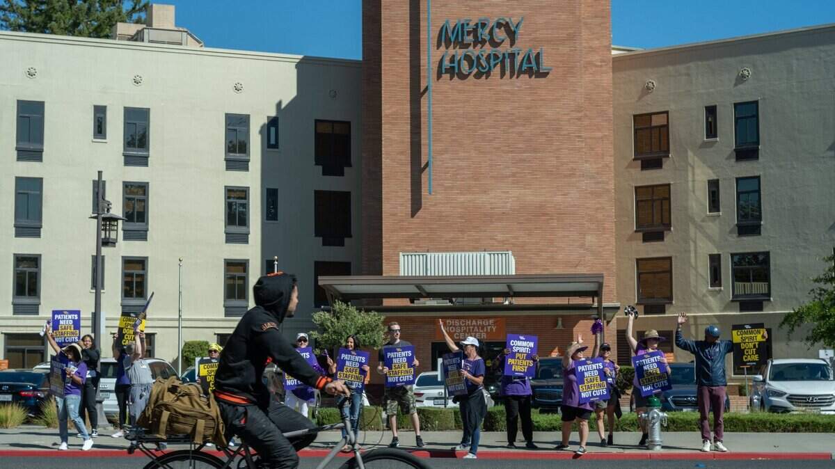 A cyclist watches as CommonSpirit healthcare workers picket outside Dignity Health Mercy General Hospital in Sacramento on Thursday, Sept. 26, 2024, in response to the outsourcing of critical jobs, layoffs and the impact on patient care. California Nurses Association announced Friday that Dignity Health nurses have ratified a new four-year contract.