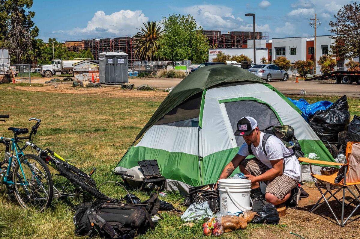 Homeless veteran David Michael Fuchs, 32, cleans up his tent at an encampment across the street from the Mercy affordable housing development in Auburn on Wednesday, April 14, 2021. Fuchs said he has been homeless for more than a year across the street from the development.