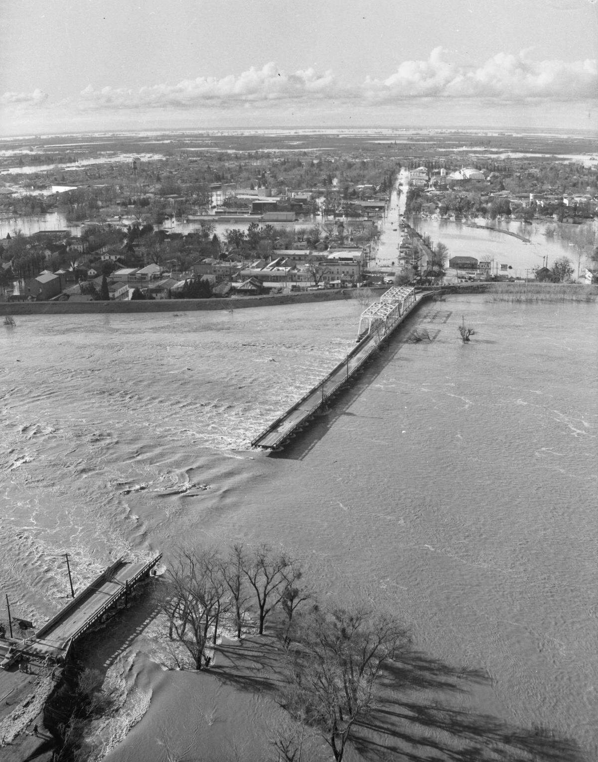 The Feather River flows between the collapsed Fifth Street Bridge between Marysville and a flooded Yuba City, background, in December 1955.