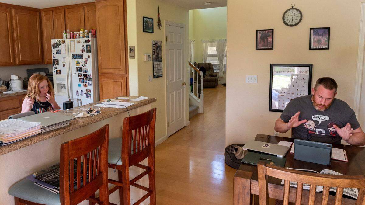 Julia Harmony, 8, left, a student at Bridgeway Island Elementary, eats a snack while she watches her father Damian, who teaches Latin at John F. Kennedy High School, record lessons from their home in West Sacramento on Thursday, Aug. 13, 2020.