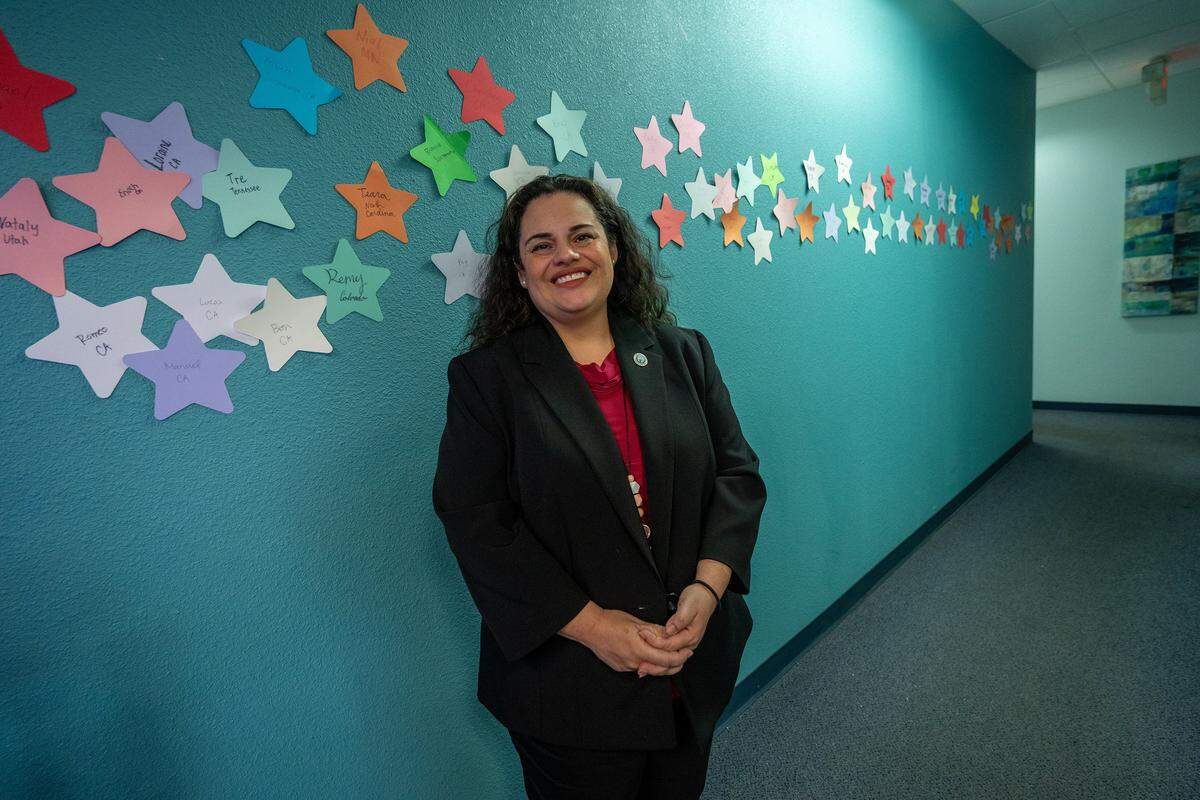 Christie Gonzales, chief operations officer for WellSpace Health, stands near a wall of stars representing lives saved at the 988 Suicide and Crisis Lifeline call center in Sacramento in December. “Each of these stars on the wall represents a life that was saved,” Gonzales said, explaining that, unlike 911, counselors stay on the line to help callers through a crisis until it is resolved.