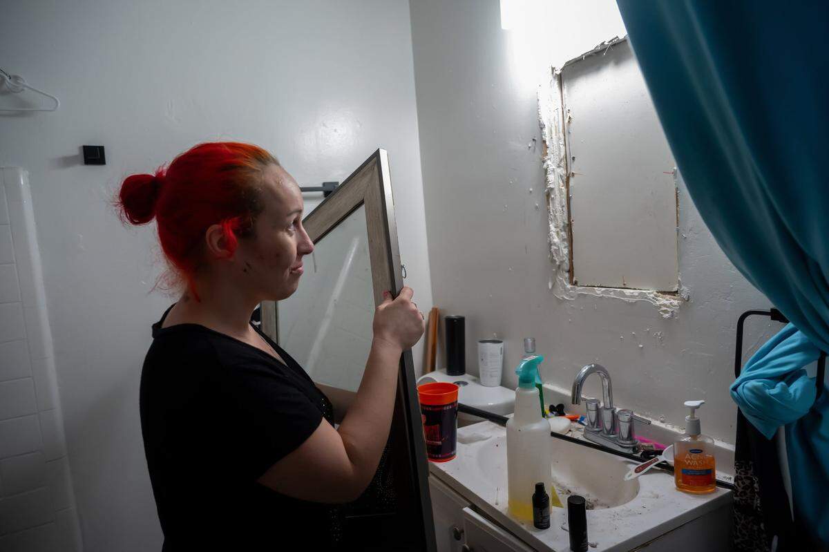 Corina Lovelace, a tenant at the Palms Apartments, shows a hole she boarded up behind her bathroom mirror Friday, Oct. 25, 2024. She said when she moved in, you could see right into the apartment next door. 