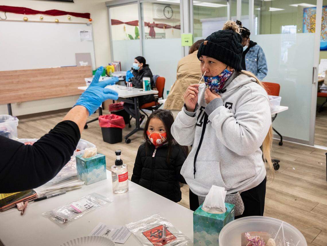 Mai Vang, of Sacramento self tests herself on Monday, Jan. 3, 2022 for COVID-19 at the La Familia Counseling Center in South Sacramento as her daughter Ella Yang, 5, waits for her test. Some people waited more than two hours in line.