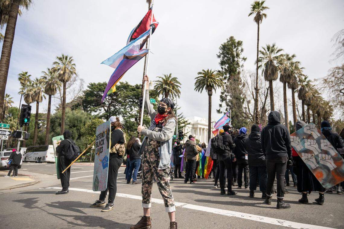 “Mama Possum” waves flags on N Street in Sacramento during a march by the Pride Was A Riot trans activist group to protest the Detransition Awareness Day event at the state Capitol on Friday.