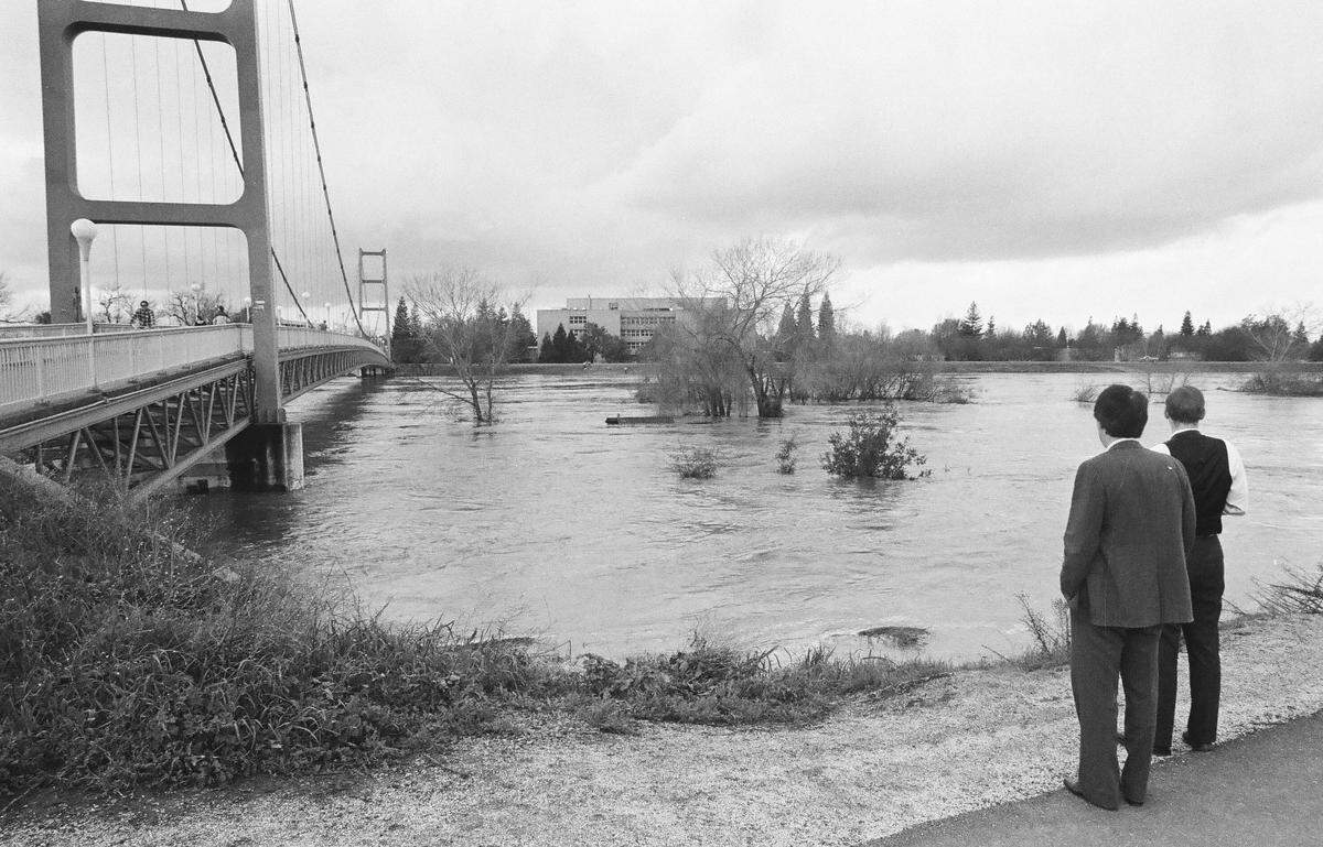 Spectators watch the high-flowing American River slide under the Guy West Bridge in Sacramento on Feb. 18, 1986. 