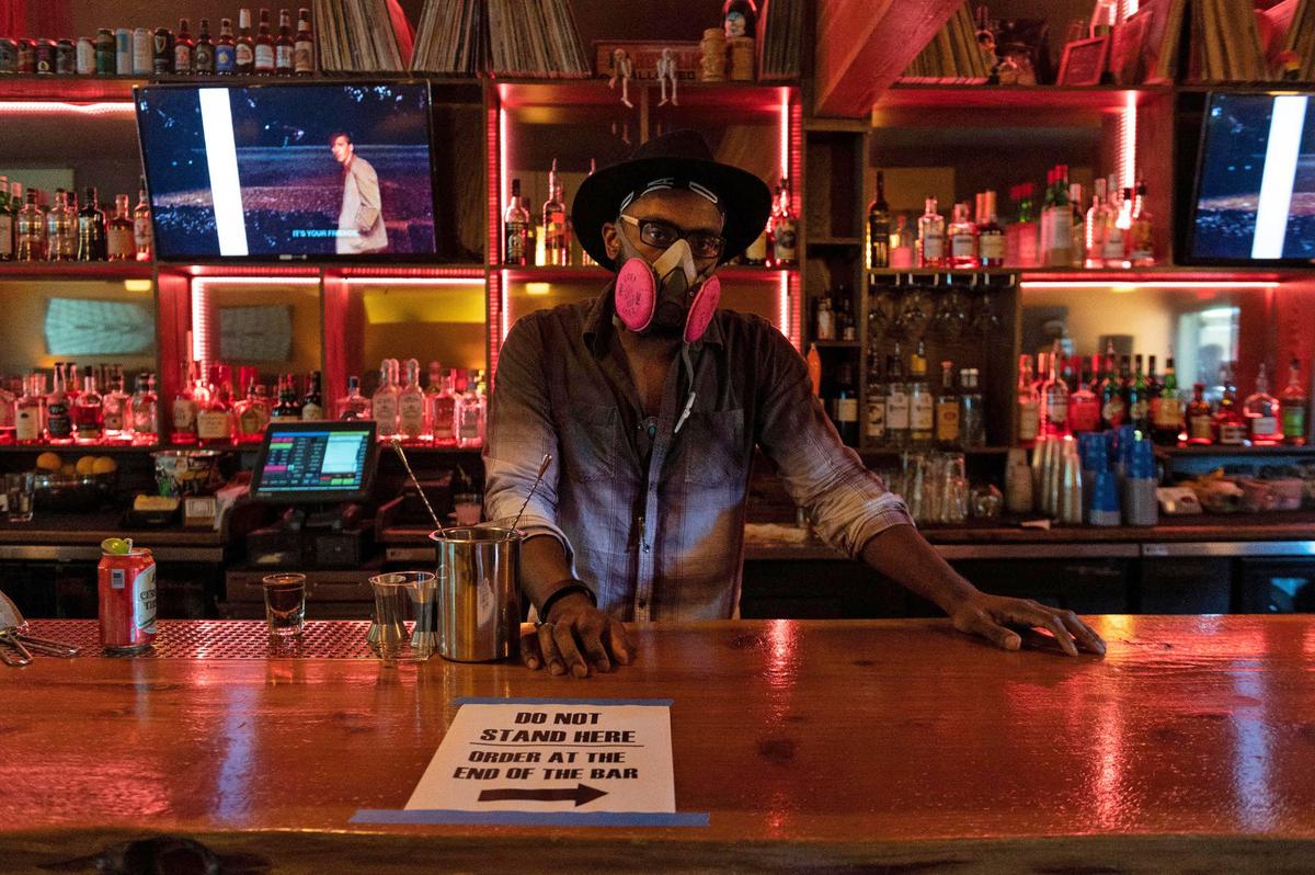 Bartender Benjamin Carter Jr. wears a respirator at B-Side as the bar reopens from its coronavirus closure on Friday, June 12, 2020. “B-Side is family,” said Carter, who has been working at the bar for more than three years. B-Side has implemented a system, described in the sign on the bar in front of Carter, instructing customers order at one end of the bar to limit the number of people inside.