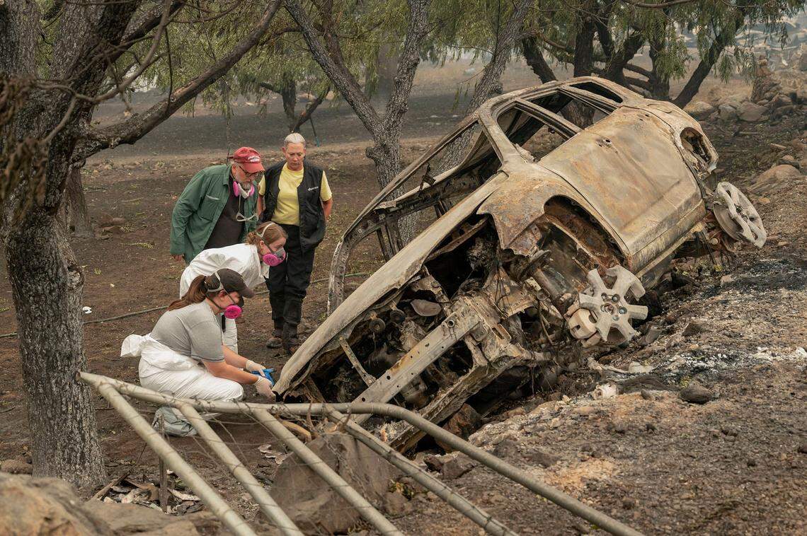 Susan Hobson, right, K9 handler, and forensics anthropologists from California State University, Chico, examine a vehicle where two people were found dead on Doggett Creek Road along Highway 96 as the McKinney Fire burns in Klamath National Forest in Siskiyou County on Monday, Aug. 1, 2022.