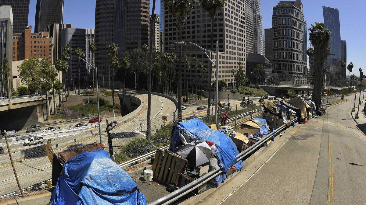 A homeless encampment on Beaudry Avenue is seen in May 2020 as traffic moves along Interstate 110 below in downtown Los Angeles. In the L.A. mayoral race, the top candidates agree homelessness is the No. 1 issue. They disagree on who should control the purse strings to deliver behavioral health and substance use treatment.