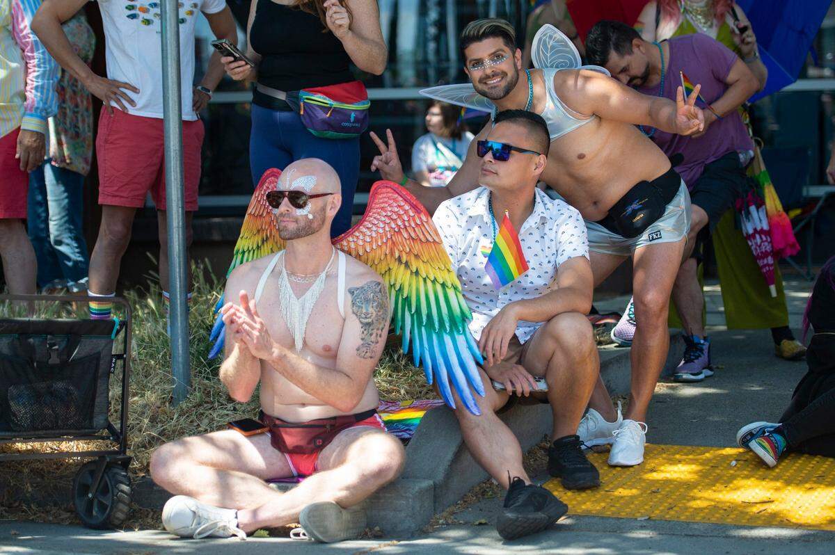 Sinan Dunlap, left, Justin Carlos, center, and Alex Liberati watch as Sacramento Pride March and Parade passes by on 10th Street during the on Sunday, June 11, 2023.