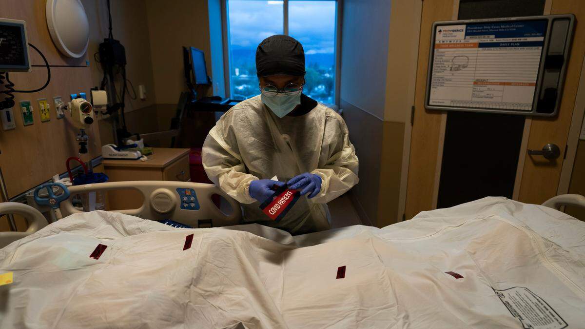 Registered nurse Bryan Hofilena attaches a “COVID Patient” sticker on a body bag of a patient who died of coronavirus at Providence Holy Cross Medical Center in Los Angeles, Tuesday, Dec. 14, 2021.