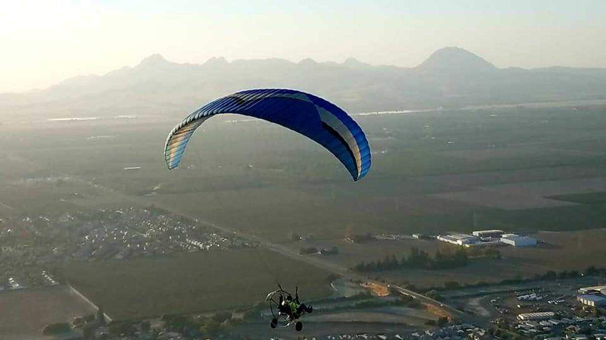 A pilot flies a paramotor with the Sutter Buttes in the distance.