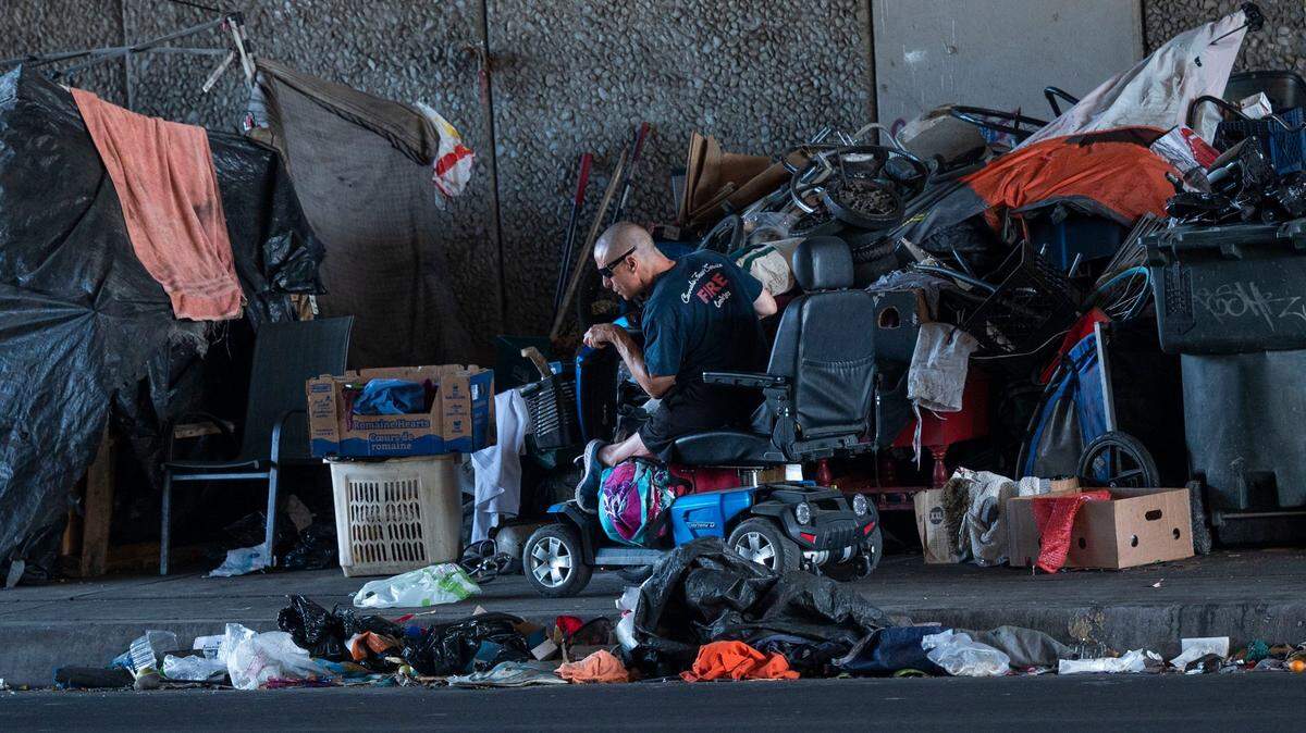 A person in a motorized wheelchair maneuvers his way past a sidewalk campsite on Broadway in Sacramento on Wednesday, Oct. 5, 2022, after a Sacramento Community Response team visited with the homeless residents. The outreach team informed the campers about a new city ordinance that requires four feet of clearance so that wheelchair users won’t be obstructed on the sidewalk.
