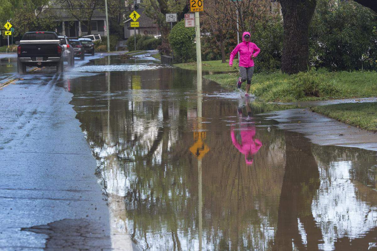 Shauna McIntosh runs along the flooded sidewalk on H Street just past 44th Street on Tuesday, March 21, 2017 in East Sacramento, Calif., as cars slow down behind her as they make their way through the rain drenched intersection.