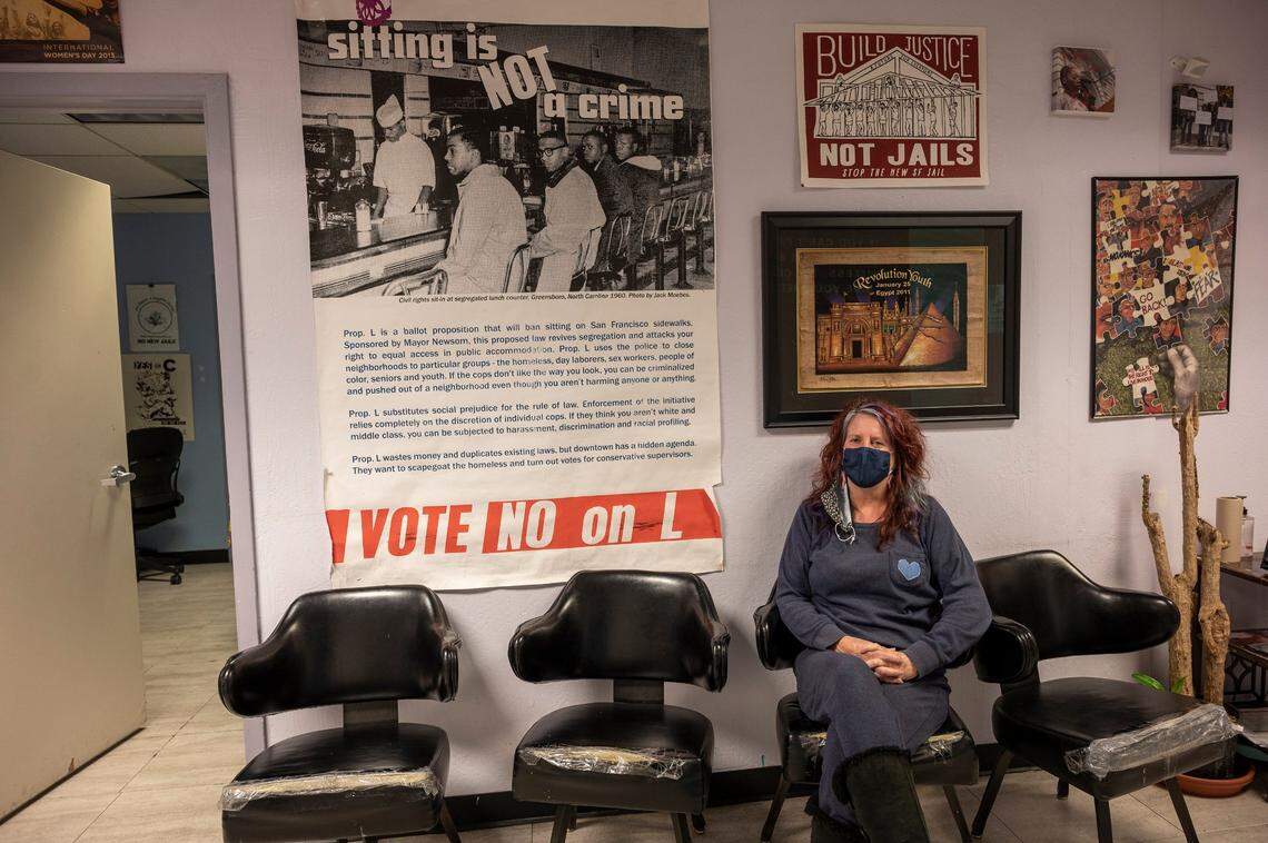 Jennifer Friedenbach, executive director of the Coalition on Homelessness, sits beneath a decade-old banner against Proposition L in San Francisco on Oct. 12. Gov. Gavin Newsom was mayor of San Francisco when the law banning sitting or lying down on city sidewalks between 7 a.m. and 11 p.m. passed in 2010.