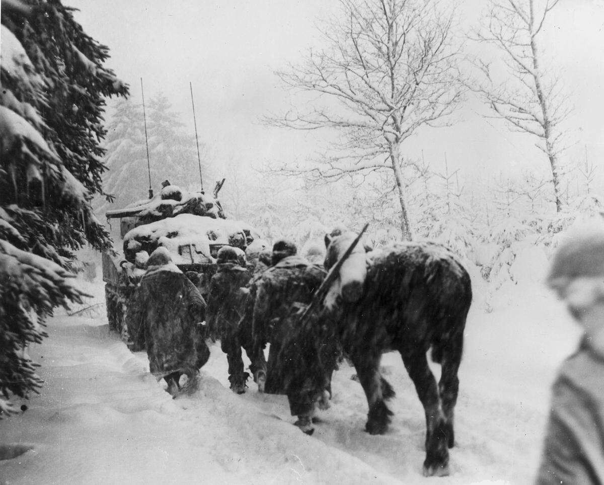 Members of the Army’s 82nd Airborne Division trudge through the snow behind a tank during the Battle of the Bulge in 1944. 