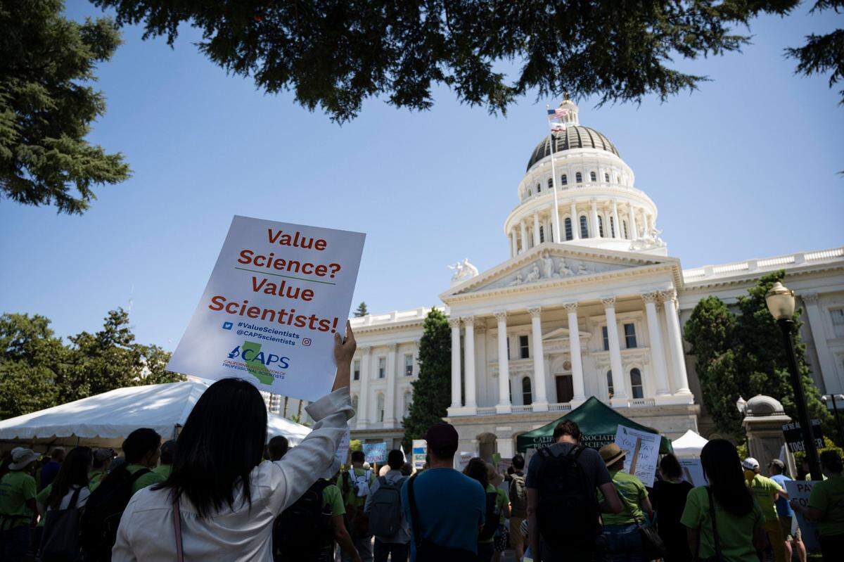 Research assistant Hong Li holds up a sign at the state Capitol on Wednesday, Aug. 30, 2023, during a rally by the California Association of Professional Scientists, known as CAPS, for increased wages.