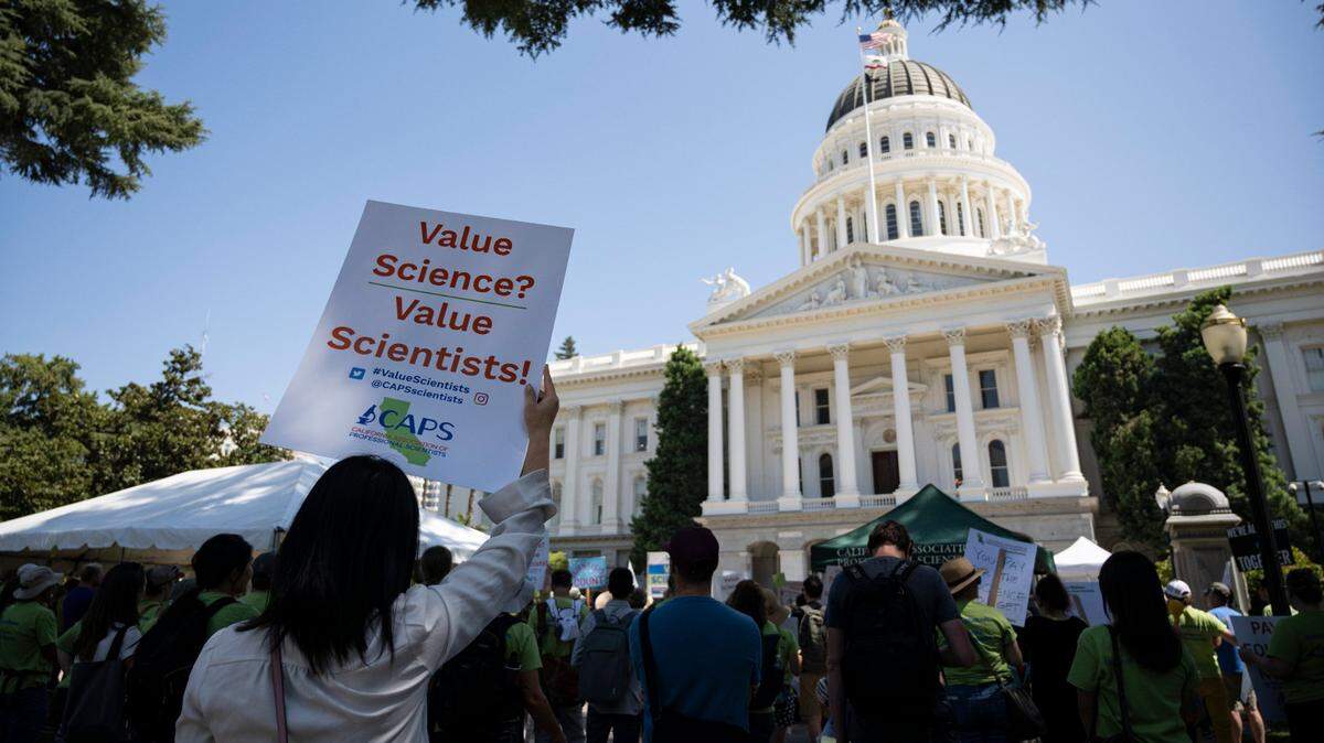 Research assistant Hong Li holds up a sign at the state Capitol on Aug. 30, 2023, during a rally by the California Association of Professional Scientists, known as CAPS, for increased wages.
