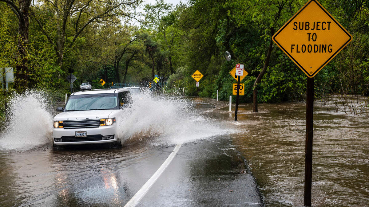 A car drives through flooding at the intersection of Winding Way and Walnut Avenue in Arden Arcade, Sunday, April 5, 2020. At right, he surface of Arcade Creek reaches the edge of the roadway.