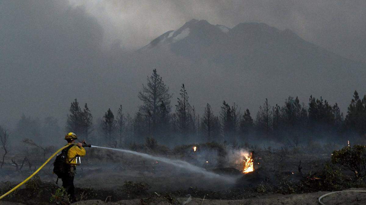 With Mount Shasta in the background, a firefighter cools down hot spots on Monday, June 28, 2021, after the Lava Fire swept through the area north of Weed, Calif.