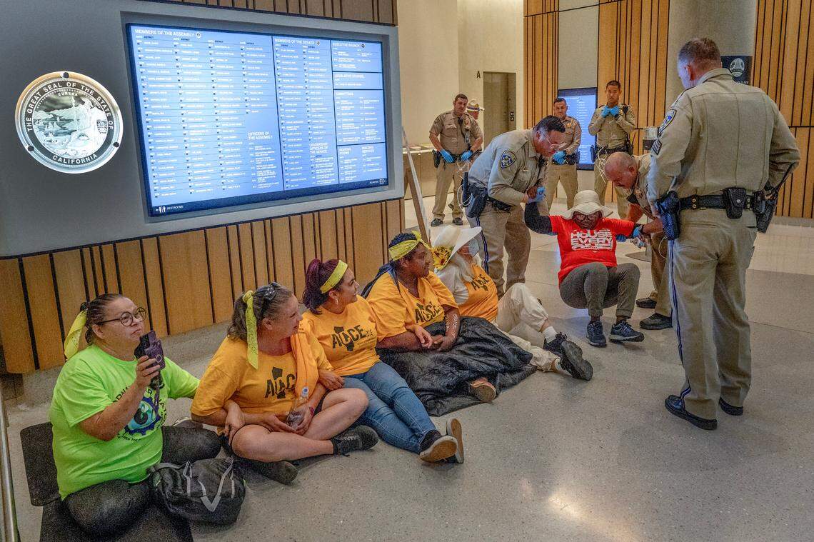 Jesus Figueroa Cacho, right, was among a group of protesters, all seated, who were arrested in the lobby of the Capitol Swing Space after a rally and march demanding affordable housing and an end to encampment sweeps on Thursday. Cacho, a nursing care worker for decades, is on disability because of her vision. She lives in her car after an eviction over fees she believes were fraudulent.