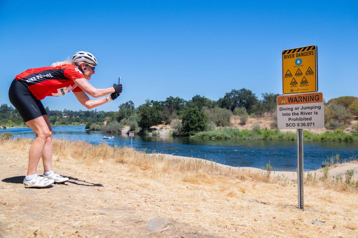 Wendy Lambert takes a photo of the new signs near the clay banks along the American River in Rancho Cordova on Friday. Lambert, who is a volunteer with the American River Bike Patrol, said she cycles almost every day and visits the area frequently.