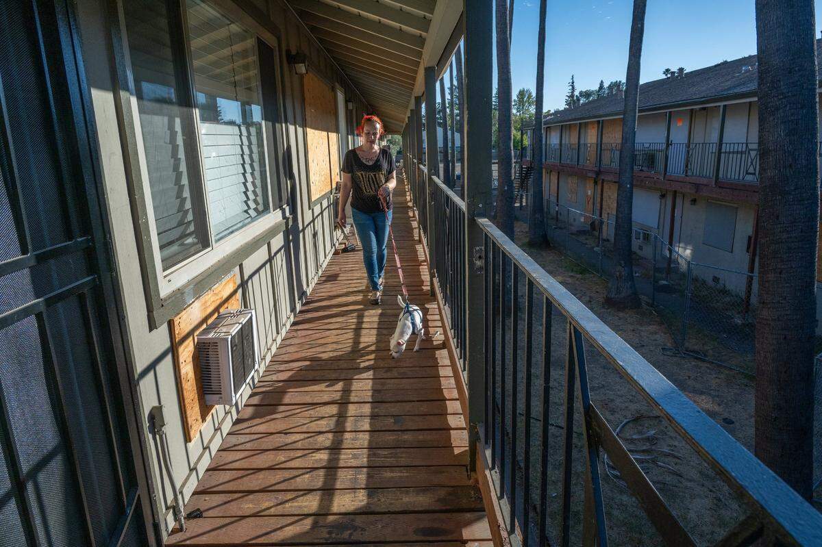 Corina Lovelace, a tenant at the Palms Apartments, walks her dog past boarded-up windows on Oct. 25, 2024, after a fire destroyed one of the buildings in the complex. Since the fire, tenants have been living in dangerous conditions, with mold, broken heaters, gas leaks, and rodent infestations.