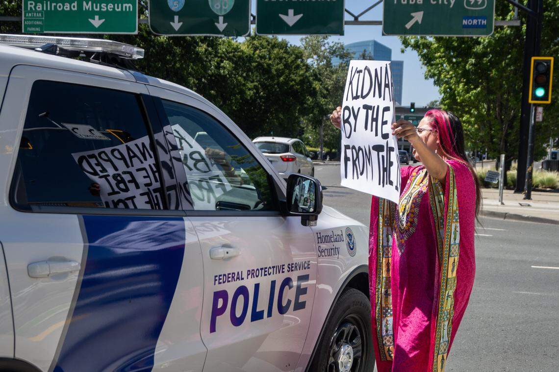 A protester puts up her poster in front of a Homeland Security vehicle outside of the Matsui Federal Courthouse where the hearing for Carlos Mendoza was held in Sacramento on Tuesday, April 14, 2026.