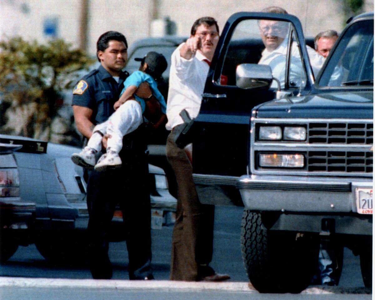 An officer holds one of the children allowed to leave the Good Guys store on April 4, 1991, after the hostage-takers were given what they thought was a bulletproof vest. The gunmen later demanded more such vests.