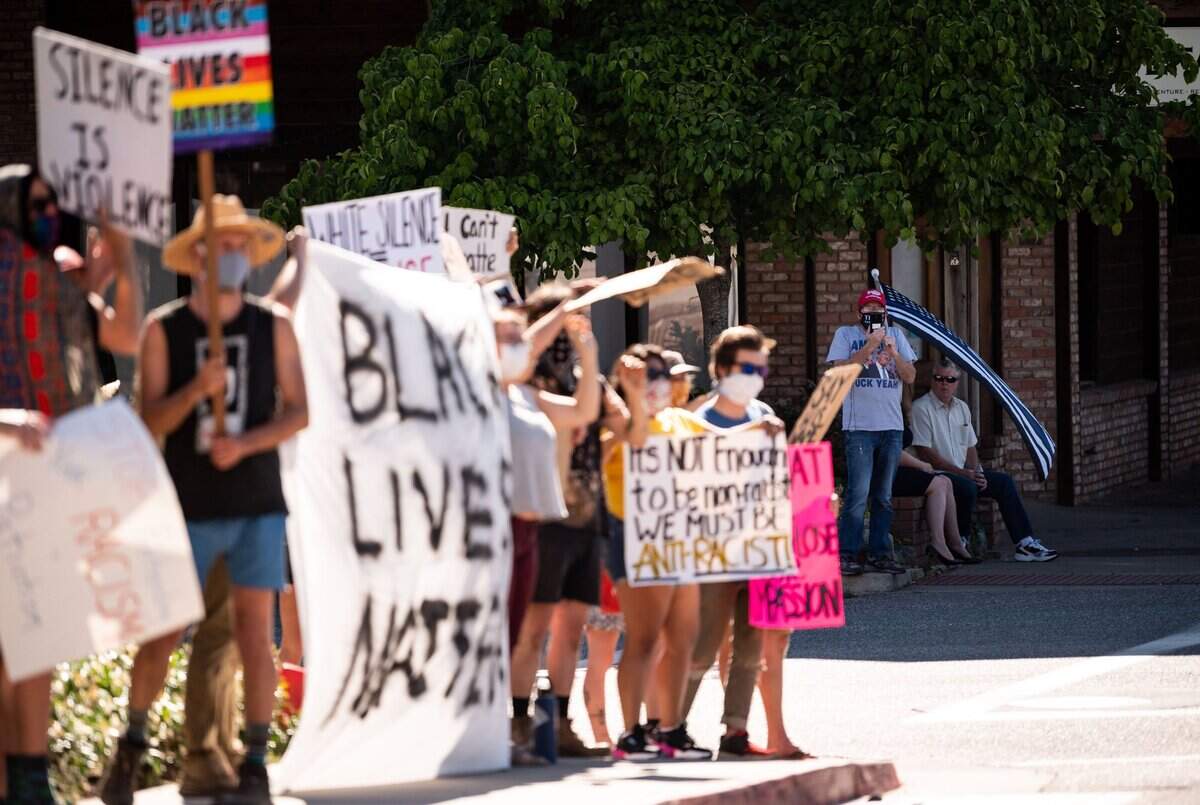 Bill White, of the Auburn area, holds a version of the U.S. flag with a blue stripe while across the street recording protesters as they rally against racism in Colfax on Wednesday, for the second time in as many weeks in the rural Placer County city.