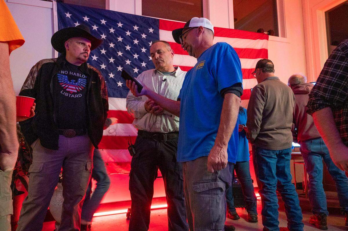 Shasta County Board of Supervisors District 2 candidate Dale Ball, center, shows his phone to District 4 Supervisor Patrick Jones as they wait for results of the election to recall District 2 Supervisor Leonard Moty on Feb. 1, in Palo Cedro. A man in a cowboy hat wears a shirt that reads “No Hablo Libtard,” at left.